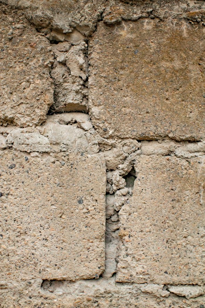 Weathered uneven aged brick wall with cement in daylight in town street on building facade