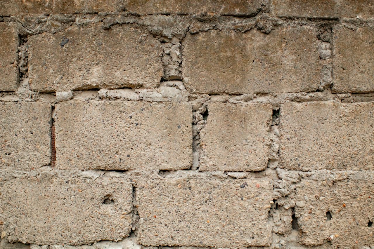 Old shabby bricks with cracks and uneven texture of wall in daytime in town street