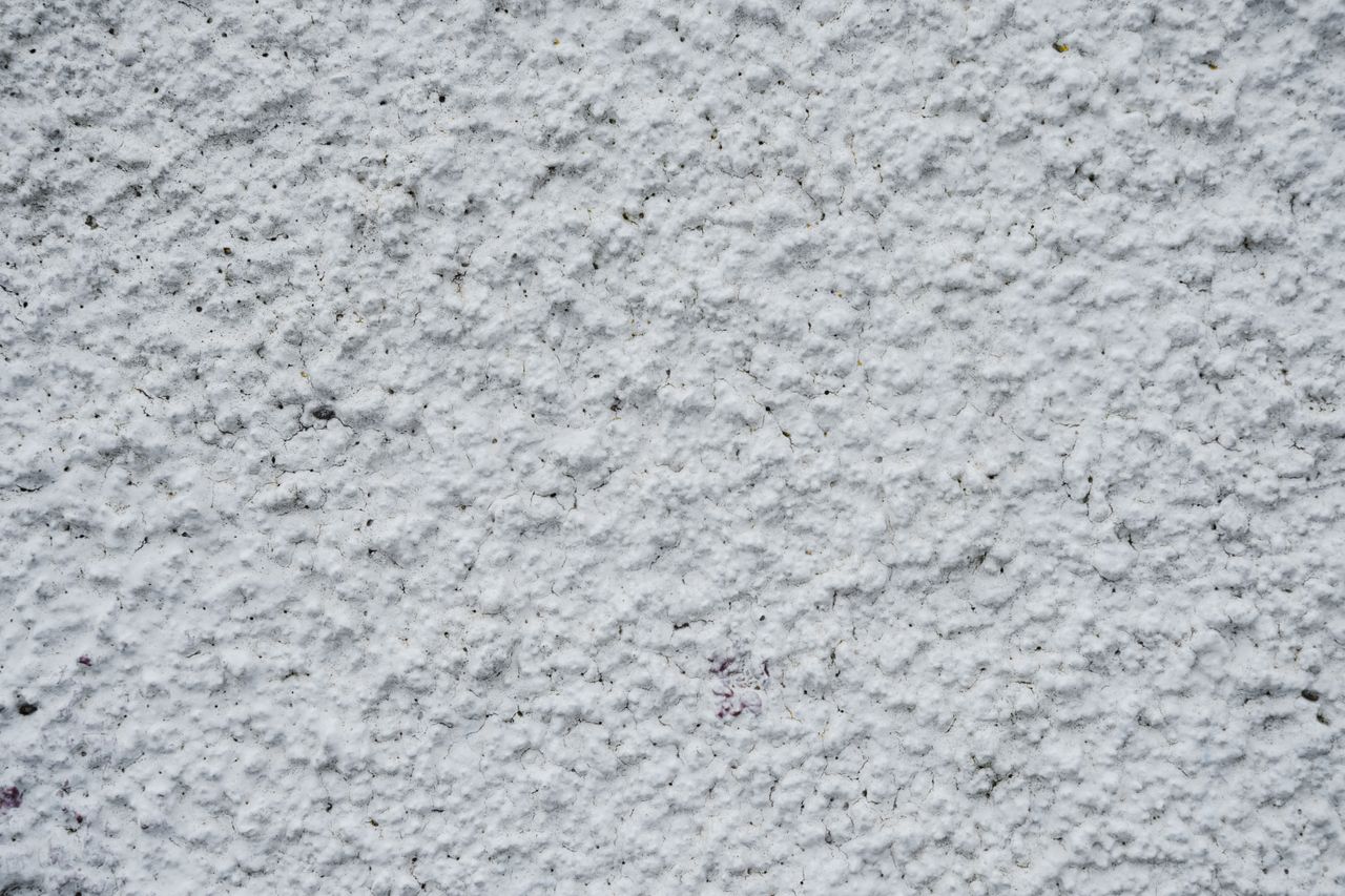 Textured white wall of old concrete building on street of town in daytime